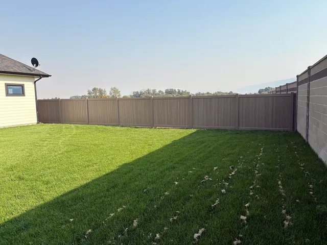 Finished brown vinyl privacy fence enclosing a green residential yard